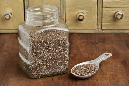 chia seeds in glass jar and on measuring aluminum tablespoon with a vintage drawer cabinet in background